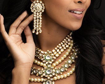 May include: A woman wearing a gold and green necklace with pearl accents and matching earrings. She is also wearing a gold headpiece with a similar design.