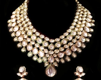 Peut inclure: Un collier et des boucles d'oreilles en or avec un motif en forme de larme. Les bijoux sont ornés de pierres précieuses blanches et rose pâle.