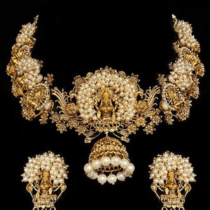 Op de afbeelding: Een gouden ketting- en oorstekerset met parel accenten en ingewikkelde bloemmotieven. De hanger heeft een klein, gedetailleerd figuurtje van een godheid.