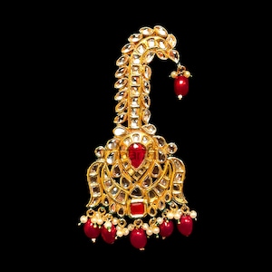 Op de afbeelding: Een gouden en rode juwelen haarornament met een gebogen ontwerp en hangende rode kralen.