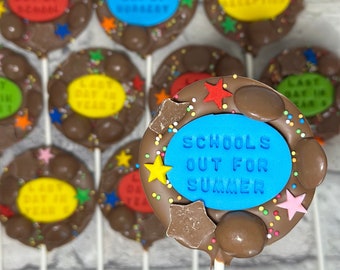 May include: Chocolate lollipops with colorful decorations and text. The lollipops have a chocolate base with a ring of chocolate candies and colorful star-shaped sprinkles. The center of each lollipop has a blue circle with the words "SCHOOLS OUT FOR SUMMER".