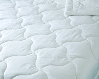 May include: A white quilted blanket with a wavy pattern. The blanket is made of a soft, textured material. The words "Organic cotton batting inside" are printed on the lower left corner of the image.