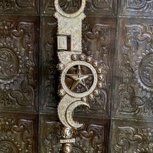 Pode incluir: Um freio de cavalo prateado e bronze com um design de estrela e lua crescente. O freio apresenta padrões gravados intrincados e um topo circular. O design central inclui uma estrela dentro de um círculo e uma forma de lua crescente.