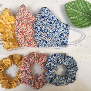 Puede incluir: Tres mascarillas de tela con estampados florales en amarillo, naranja y azul, y tres scrunchies a juego.