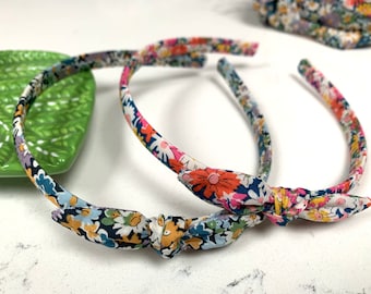 May include: Two floral patterned headbands with a knotted bow detail. The headbands are made of a soft fabric with a variety of colors, including pink, blue, yellow, and green.