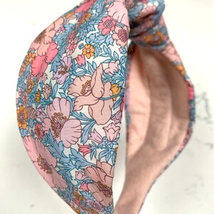 May include: A pink and blue floral patterned headband with a knotted design. The headband is made of soft fabric and has a comfortable fit.