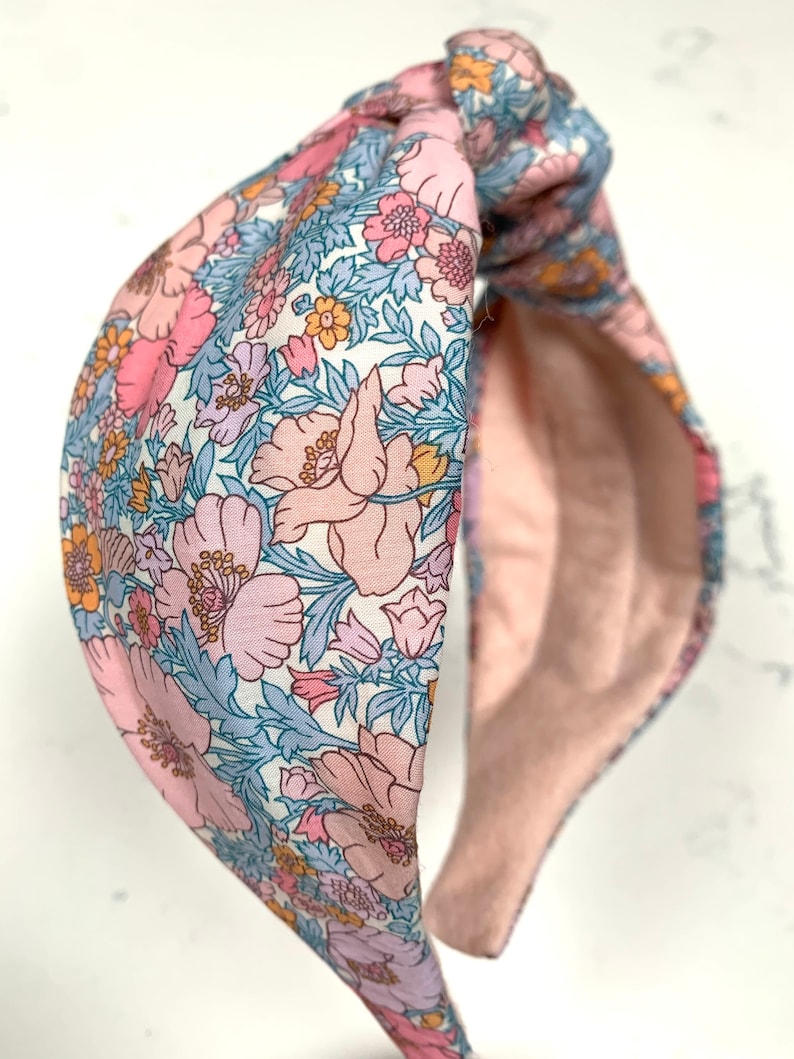 May include: A pink and blue floral patterned headband with a knotted design. The headband is made of soft fabric and has a comfortable fit.