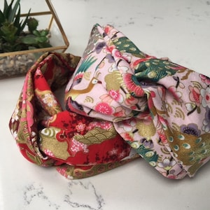 Puede incluir: Una diadema de tela rosa y roja con un diseño anudado. La tela presenta un patrón floral y de pájaros.