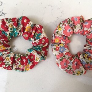 May include: Two floral print scrunchies, one with red and white flowers and the other with pink and white flowers.