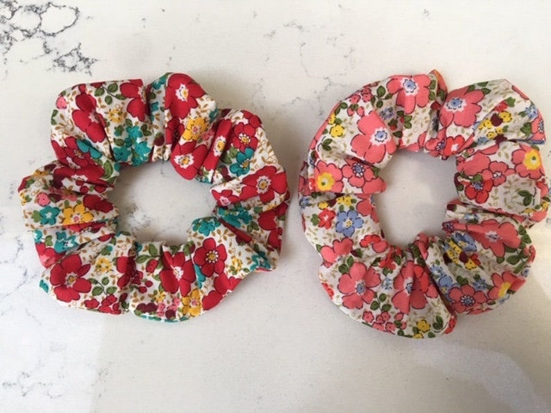 May include: Two floral print scrunchies, one with red and white flowers and the other with pink and white flowers.