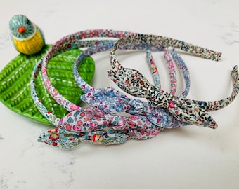 May include: Four floral patterned headbands with a bow at the end of each headband. The headbands are arranged in a stack with the bow of each headband facing the viewer.