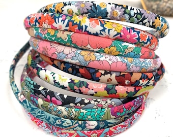 May include: A stack of colorful floral patterned headbands. The headbands are made of fabric and are in various shades of pink, blue, green, and yellow.