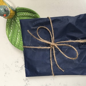 May include: A navy blue gift wrapped with twine and tied in a bow. The gift is sitting on a white surface with a green ceramic bird figurine.