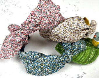 May include: Three fabric headbands with knotted bows. The headbands are in floral patterns: pink and white, brown and white, and blue and white.