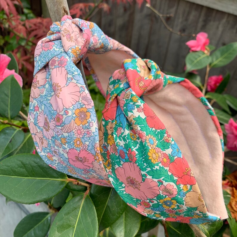 May include: Two floral patterned fabric headbands with a knotted design. One headband is pink and blue with a white background, the other is green and pink with a white background.