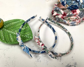 May include: Two floral patterned headbands with a bow on each end. The headbands are on a white surface with a green leaf-shaped dish.