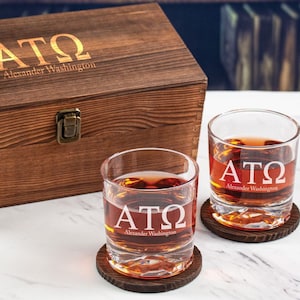 May include: Two clear glass whiskey tumblers with the letters ATO and the words "Alexander Washington" engraved on them. The glasses are sitting on wooden coasters and are in front of a wooden box with the same engraving.