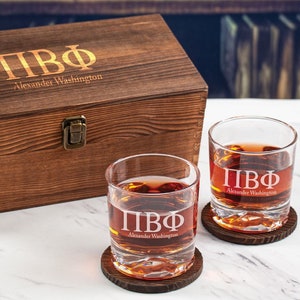 May include: Two engraved glass tumblers with the letters "ПВФ" and "Alexander Washington" on a wooden coaster. The tumblers are filled with a dark liquid. A wooden box with the same engraving is in the background.