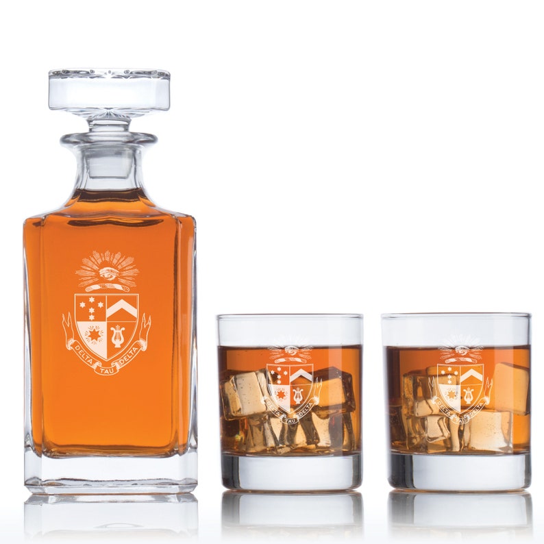 May include: A set of three clear glass decanter and glasses with a crest featuring a lyre, stars, and the text "Delta Tau Delta".