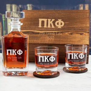 May include: A wooden box set with a decanter and two glasses. The box, decanter, and glasses are engraved with the letters "ПКФ" and the text "My Greek Life 2023".
