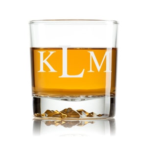 May include: A clear glass rocks glass with a gold rim and a textured bottom. The glass is filled with amber liquid and has the letters "KLM" etched on the side.