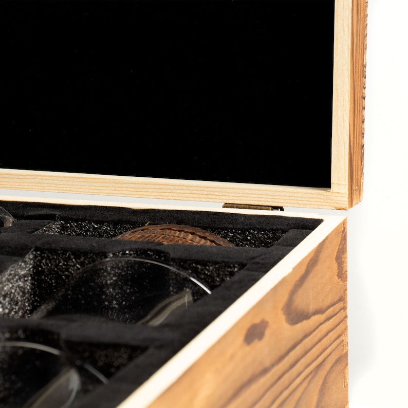 May include: A wooden box with a hinged lid, partially open, revealing a black velvet interior. The box is lined with black foam and contains several clear glass cups.