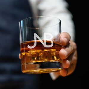 May include: A clear glass with ice and amber liquid. The glass has the initials "NB" etched on the side.