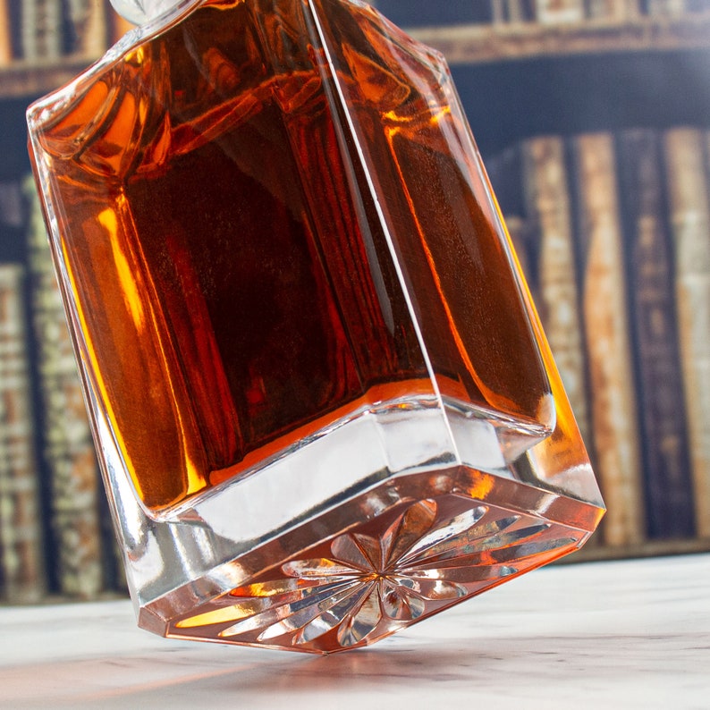May include: A clear glass decanter with a faceted bottom and a dark amber liquid inside. The decanter is tilted and the bottom is visible.