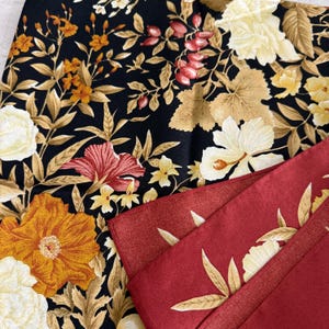 K&ouml;nnte beinhalten: Nahaufnahme von zwei Stoffen mit Blumenmuster. Einer ist schwarz mit orangefarbenen, gelben und wei&szlig;en Blumen und goldenen Bl&auml;ttern. Der andere ist rot mit einem goldenen und wei&szlig;en Blumenmuster. Die Stoffe sind gefaltet und geschichtet.