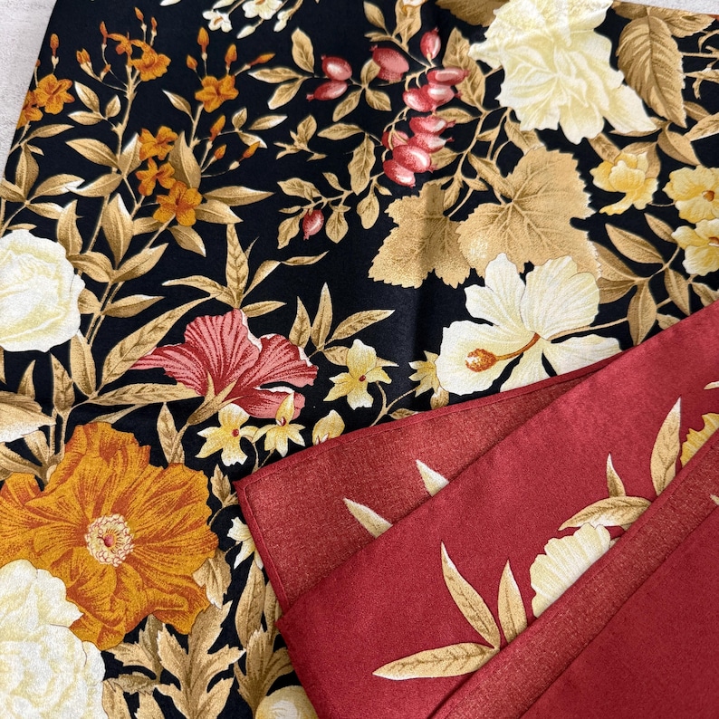 K&ouml;nnte beinhalten: Nahaufnahme von zwei Stoffen mit Blumenmuster. Einer ist schwarz mit orangefarbenen, gelben und wei&szlig;en Blumen und goldenen Bl&auml;ttern. Der andere ist rot mit einem goldenen und wei&szlig;en Blumenmuster. Die Stoffe sind gefaltet und geschichtet.