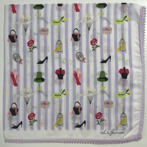 May include: A white and purple striped fabric with a repeating pattern of hats, birds in cages, purses, roses, and shoes. The fabric has a lavender crochet trim and the text "Laura Guinness" is printed in the bottom right corner.