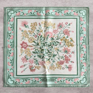 May include: A square scarf featuring a central bouquet of pink and yellow flowers with green foliage on a white background. The border is a light green frame decorated with a repeating pattern of small pink flower buds and the text JIM THOMPSON.