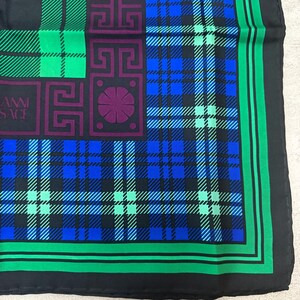 May include: A black silk scarf with a plaid pattern in shades of blue, green, and black. The scarf features a square design with geometric shapes in purple and the text "GIANNI VERSACE". The border is green.