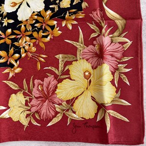 K&ouml;nnte beinhalten: Quadratisches rotes Seidentuch mit floralem Design. Der Schal zeigt gelbe, rosa und wei&szlig;e Hibiskusbl&uuml;ten mit einem schwarzen Abschnitt mit kleineren orangefarbenen Bl&uuml;ten. Die Signatur Jim Thompson befindet sich unten rechts.