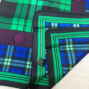 May include: A silk scarf with a plaid pattern in shades of green, blue, and black. The scarf features geometric designs in purple and green. The edges are bordered with a green and black stripe.