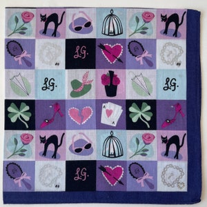 May include: A purple and blue patterned bandana with a repeating design of hearts, cats, sunglasses, clovers, and other symbols. The bandana has the letters "L.G." printed in white on a black background.