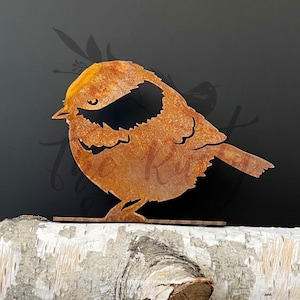 Könnte beinhalten: Eine rostige Metallsilhouette eines Vogels mit rundem Körper und kurzem Schwanz. Der Vogel steht auf einem kleinen, flachen Sockel.