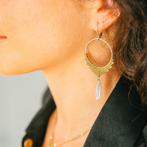 May include: Gold hoop earrings with a dangling silver leaf charm. The earrings are made of small beads and have a delicate, bohemian style.