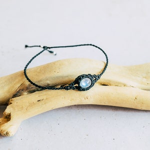 May include: A black macrame bracelet with a round, iridescent moonstone bead.
