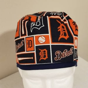 May include: A Detroit Tigers baseball team scrub cap. The cap features a navy blue and orange color scheme with the team's logo, baseballs, and the word "Detroit" printed on it. The cap has a navy blue band.