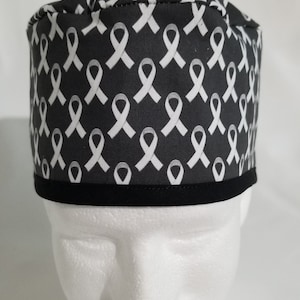 May include: A black and white patterned cap featuring white awareness ribbons on a dark background. The cap has a black band around the bottom edge. The cap is displayed on a white mannequin head.