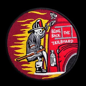 May include: A circular embroidered patch featuring a skeleton firefighter in a helmet and gear standing on the back of a red fire truck. The background is a yellow and red flame design. The text on the truck reads "BRING BACK THE TAILBOARD".