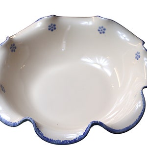 May include: A white ceramic bowl with a ruffled edge and a blue trim. Small blue floral designs are evenly spaced around the rim. The bowl has a shallow, open design.