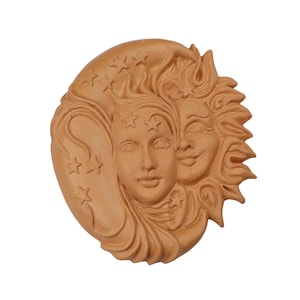 May include: A terracotta wall plaque depicting the sun and moon as faces. The sun is on the right and has a smiling face with rays emanating from its head. The moon is on the left and has a more serious expression with stars around its head.