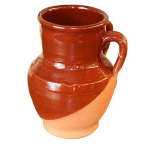 May include: A brown ceramic jug with two handles. The upper part is a darker brown, the lower half a lighter clay colour. The jug has a rounded body and a wide opening, ideal for serving drinks. The height is approximately 20 cm.