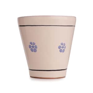 Puede incluir: Jardinera de cerámica color crema con forma ligeramente acampanada. La jardinera presenta dos rayas horizontales negras y dos diseños florales azules. El borde es de color rosa claro. La base es de color terracota.