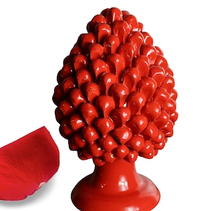 May include: A bright red ceramic pine cone ornament with a smooth, glossy finish. The pine cone is sitting on a base and has a detailed, textured design.