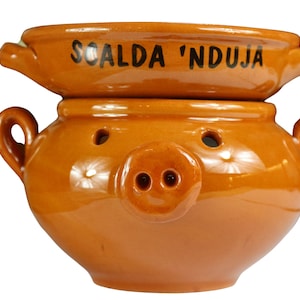 Può includere: Un vaso in terracotta a forma di maiale con una ciotola più piccola sopra. La ciotola ha la scritta "Scalda 'Nduja".
