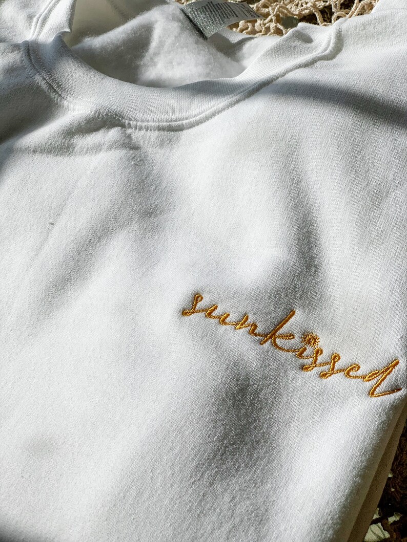 May include: White sweatshirt with the word "sun-kissed" embroidered in gold thread.