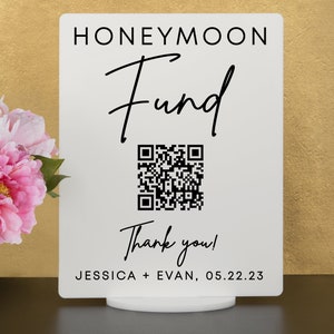 May include: White sign with black text that reads "Honeymoon Fund" with a black and white QR code and the text "Thank you!"  Below the QR code is the text "Jessica + Evan, 05.22.23"